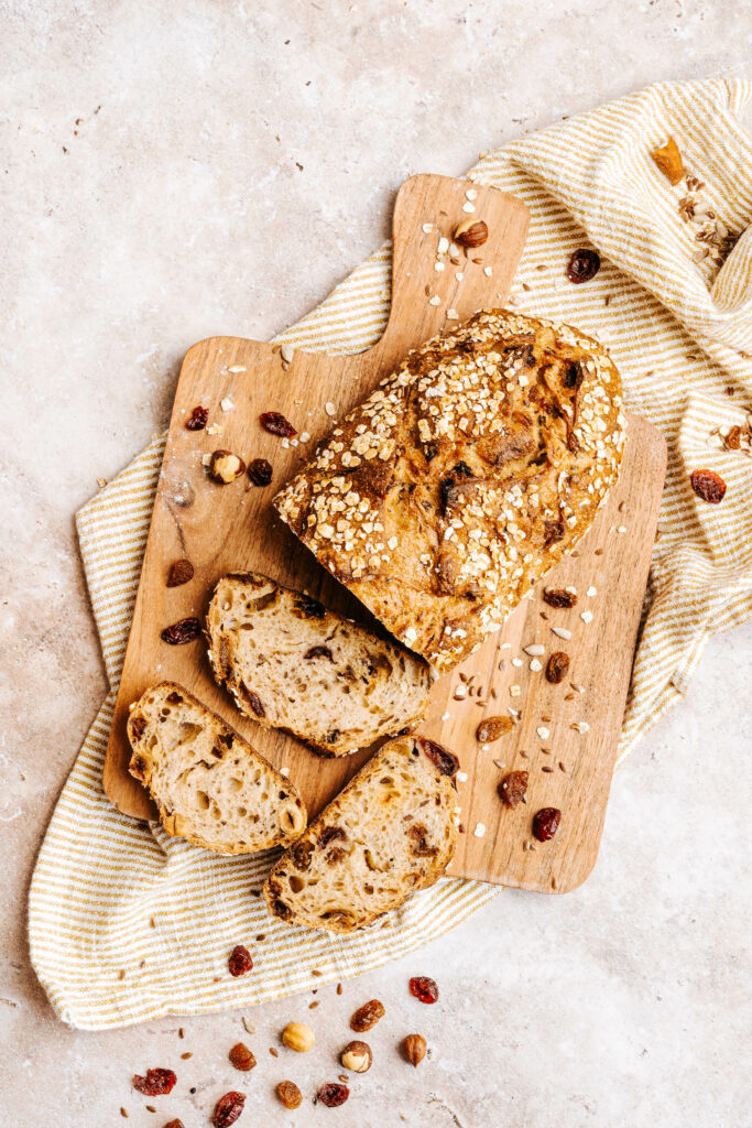 Photo du pain muesli tranché avec flocons d'avoines et des raisins secs sur une planche lui-même sur un torchon.